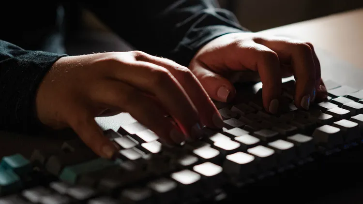 Persona escribiendo siniestramente en un teclado oscuro.