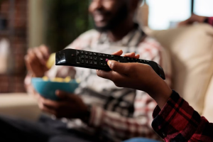 MUJER SOSTENIENDO CONTROL REMOTO DE TV CON HOMBRE AL FONDO